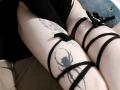 TempleWydner's pale thighs with black strappy lingerie, featuring spider tattoos, sitting with legs crossed, showing a detailed black spider tattoo on the right thigh.