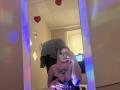 DiLaria with rainbow lights on her hands and chest tattoo, taking a mirror selfie showing her big boobs, wearing a black strap top, in a room with a blue glow.
