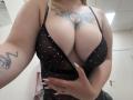 Les seins volumineux et pulpeux de DiLaria, vêtue d'une robe noire transparente à pois, dévoilent un tatouage de soleil entre ses seins et un tatouage d'araignée sur son bras droit..
