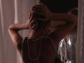 RosaVance, back to camera, hands in blonde hair, wearing a pearl necklace, no top, reflection in mirror, dim lighting, bare shoulders, slightly blurred, sexy, intimate.