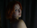 MasakoParkey has red hair, blue eyes, and is looking over her shoulder with a slight smile, showing her bare shoulder and a small freckle on her cheek.