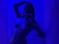 Blue-lit selfie of Molray, nude, with hand in hair, holding phone, covering tits, showing pussy, standing against white wall, in dim room. Molray's phone case is visible.