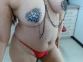 LizethBells, topless with sparkly nipple pasties, wearing red thong, chain hanging between tits, small pink butt plug, light skin, in a room with a dresser.