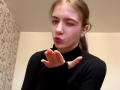 EviaMarcot with puffy red lips, winking, and making a kissy face, wearing a black turtleneck, hand up, in a selfie. She has acne on her right cheek.