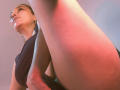 AmberDemons, legs spread, showing her ass, wearing a black dress, looking up, mouth slightly open, with a shiny lip gloss, and gold earrings, in a low-angle shot.