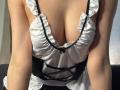 MeganCarlson's cleavage in a white, ruffled, black-trimmed maid outfit, showing her large, soft tits. She's leaning forward, arms resting on a dark surface.