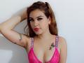 HotDemonsLatinn with brown hair, pink lace bra, tattoos on arm and chest, hand in hair, red lipstick, white wall background, wearing "Victoria's Secret" straps. Boobs, tits, pink bra.