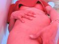 IssisDiosa's red shirt is lifted, exposing her bare belly and hand covering her pussy, while the other hand holds her flaccid cock. Her skin is pink from the lighting.