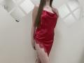 Nesie in a red satin dress with lace side, long brown hair, hand on chest, standing with a slight side angle, showing her ass and thigh in the shot.