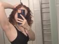 ChayaParrett with curly red hair, black tank top, holding phone in front of face, arm raised, showing armpit, small tits, mirror selfie, silver ring on right hand.