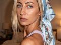 ViktoriiaLu with blue floral headscarf, looking over shoulder, showing off her tits in a lilac lace tank top, blue eyes, blonde hair, and a serious face.