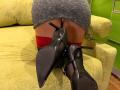 MiraGi's ass, in a gray skirt, is exposed, showing red lace stockings and black high heels with pointed toes, positioned on a green couch.