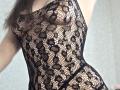 Strogoff in black lace mesh dress, exposing her tits and nipples, with a pattern of flowers and hearts. Her brown hair is visible on the left.