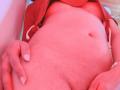 IssisDiosa's red-tinted, slightly chubby belly with visible skin texture, a small navel, and a hand with white nails resting on her right side. Her red top is partially visible.