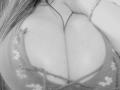 Black and white photo of MissGilliSquirty's large, round tits in a floral, lace bra. Visible cleavage with straps falling off shoulders. Slightly blurry. Breej photo watermark.