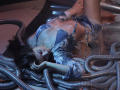StellaLewin, with her tits exposed, lies on metallic hoses, wearing a torn, blue tie-dye shirt and frayed shorts, her ass slightly raised, eyes closed, in a reflective, silver pool.