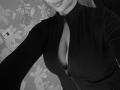 Olieri's black zip-up shirt is unzipped to reveal her big, perky tits. She's wearing a high-neck, and her lips are slightly curved in a subtle smile.