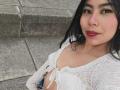 CataMoreno has dark hair, a nose ring, and wears a white lace top, showing her tits, with pink lipstick and a subtle smile, sitting on stone steps.