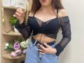 Rioria with tits in a black sheer off-shoulder top, blue high-waisted jeans, and a black belt, holding her finger to her lips, with long brown hair.