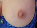 De onbedekte borsten van FrenchShanna, met een kleine, roze tepel en een licht verhoogde areola, zichtbaar onder een blauwe kanten bh. De bh heeft een groene steen aan de linkerkant..