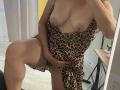 AlexisLovelyy with big tits in a leopard dress, one leg up, hand covering her pussy, mirror selfie, showing her tan lines and red nails.