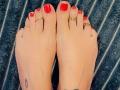 FrenchShanna's feet with red-painted toenails, gold toe rings on each toe, and a small heart tattoo on the left ankle, sitting on a dark blue, textured rug.