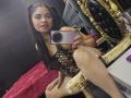 EmilyVidal with long black pigtails, wearing a black fishnet bodysuit, sitting on a gold chair, holding a glittery phone, showing her red-nailed hand and legs, reflecting in a mirror.