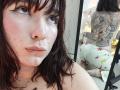 ValeriHairy69 has wet brown hair, fair skin with freckles, and a nose piercing. Her tattooed back shows a dragon, and she's wearing star-patterned panties, sitting on the floor.