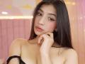 NaiaSanders has long black hair, brown eyes, and pink lipstick, looking at the camera with a slight smile. She's topless, with black straps off her shoulders, and her hand touches her cheek.