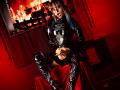 TatsumiLee in shiny black latex outfit with long sleeves and thigh-high boots, sitting on red cloth, hands on crotch, red light, fire in background, glasses, blue hair, tongue out.