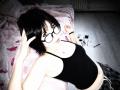 ChantellHoulihan with black glasses, short black hair, wearing a black tank top, showing her small tits, lying on a bed, looking up, with makeup and a pen nearby.