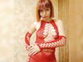 LaylaHottyX with red bob, wearing red fishnet dress, exposing her tits, and red fingerless gloves, standing in a room, looking at the camera with a slight smile.
