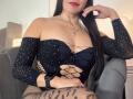 VivienneWest with long black hair, wearing a black sparkly top with cutout sides, exposing her boobs, and black tiger-patterned leggings, sitting in a gray chair.