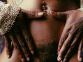 DaniaMarcell's dark brown hands spread her pussy, showing a belly button piercing and a hairy pubic area. She wears a gold, beaded wrist accessory.