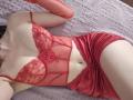 Rozalin wearing red lace lingerie and matching red satin shorts, lying on a bed with a pink textured blanket, showing her pale skin and small, perky tits.