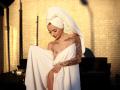KayaBelle with a white towel wrapped around her, exposing her tits, and a towel on her head, has tattoos on her arm and chest, standing in sunlight.
