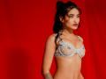 KarolPalacios with dark hair in a ponytail, wearing a light blue, sheer lace bralette, exposing her small tits, and a tattoo on her left arm, against a red background.