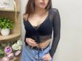 Rioria with small tits, wearing a sheer black top, blue jeans, and a black belt, has brown hair, pink lips, and a hand on her belly.