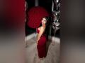 MiilaWx with big ass in a red, backless dress, standing in front of shiny silver balloons and a red rose ball, looking over her shoulder with black hair.