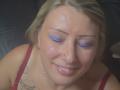 AmandalaFrancaise with blonde hair, purple eye makeup, and a nose piercing, has cum on her face, smiling, wearing red lingerie, and a tattoo on her right shoulder.