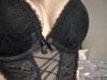Anshante's black lace lingerie with a deep V-neck, featuring a small black bow in the center and crisscross mesh detailing. Her tits are prominently displayed in the fabric.