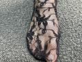 Tattiya's foot is covered in black, see-through lace with floral patterns, showing her toes through the fabric. She's standing on a textured gray carpet.