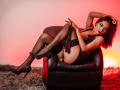 CrystalWright with black lingerie, garter, and stockings, sitting on a leather chair, holding a black paddle, wearing sparkly heels, red lighting, and a sexy, confident look.