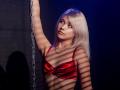 DataSley with platinum blonde hair, wearing a shiny red bra, arm raised, holding a chain, shadow stripes on her tits, looking to the side, blue light in background.