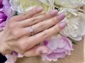 OliviaGrandas Hand mit rosa Nagellack, ein silberner Ring mit einem kleinen Diamanten und weiße, rosa und lila Blumen im Hintergrund..