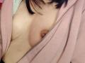 IssisDiosa's bare tits with a small, brown nipple showing through a partially zipped pink hoodie. Her black hair is visible at the top.