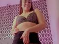 MadisonKoper with medium tits in a leopard print bra, smiling, black skirt, hand on belly, standing, pinkish room, patterned curtain, casual, confident, attractive.