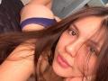 SophiaMarx with brown hair, looking at camera, wearing blue lace panties, lying on bed, showing her ass, pouting with pink lips, brown eyes, slightly flushed, sexy.