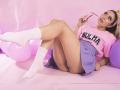 Ninilovee está acostada con las piernas levantadas, vistiendo una camisa rosa de Bulma, una falda azul, calcetines blancos y sosteniendo unas gafas rosas, mostrando su trasero y un tatuaje en su muslo..
