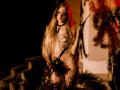 Naked MiaMeowa with long blonde hair, wearing gold chain jewelry and a black collar, holding a whip, standing on stone steps, illuminated by red and orange lights.